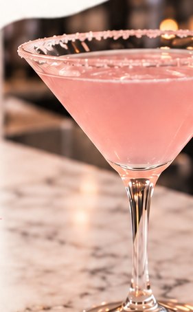 A pink martini with a sugared rim on a marble bar